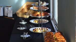 Une table de buffet proposant diverses pâtisseries et pains, disposés sur une table près d’une fenêtre.
