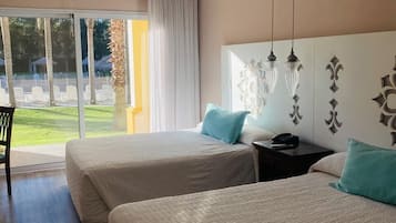 Habitación de hotel con dos camas, ventilador de techo, equipo de aire acondicionado, mesita de noche y vista a un patio.