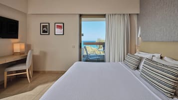 Habitación de hotel con una cama grande, un escritorio con silla, un televisor montado en la pared y un balcón con vistas al mar.