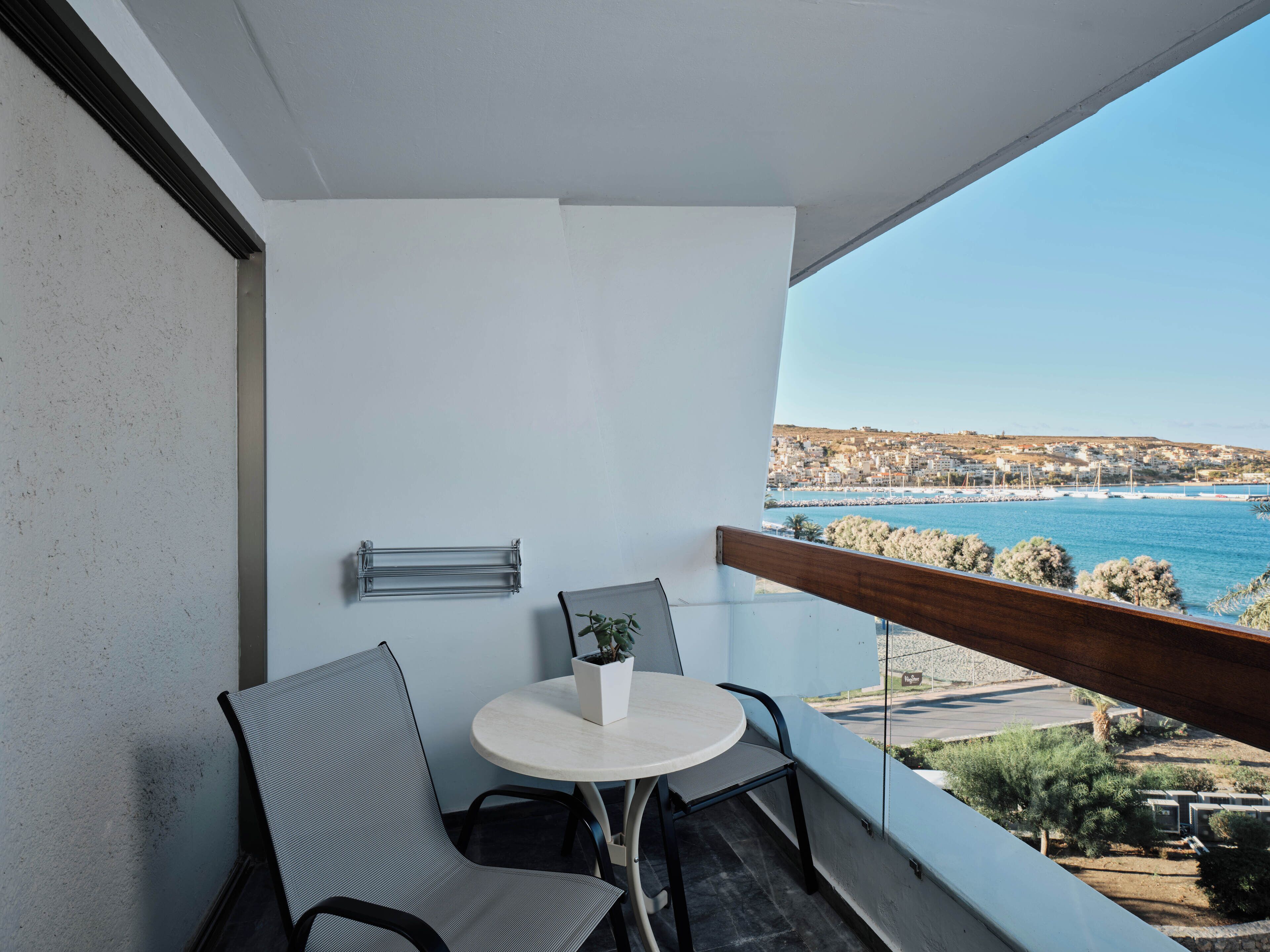 A balcony with a round table, two chairs, a small potted plant, and a view of a coastal town.