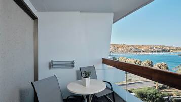 A balcony with a round table, two chairs, a small potted plant, and a view of a coastal town.