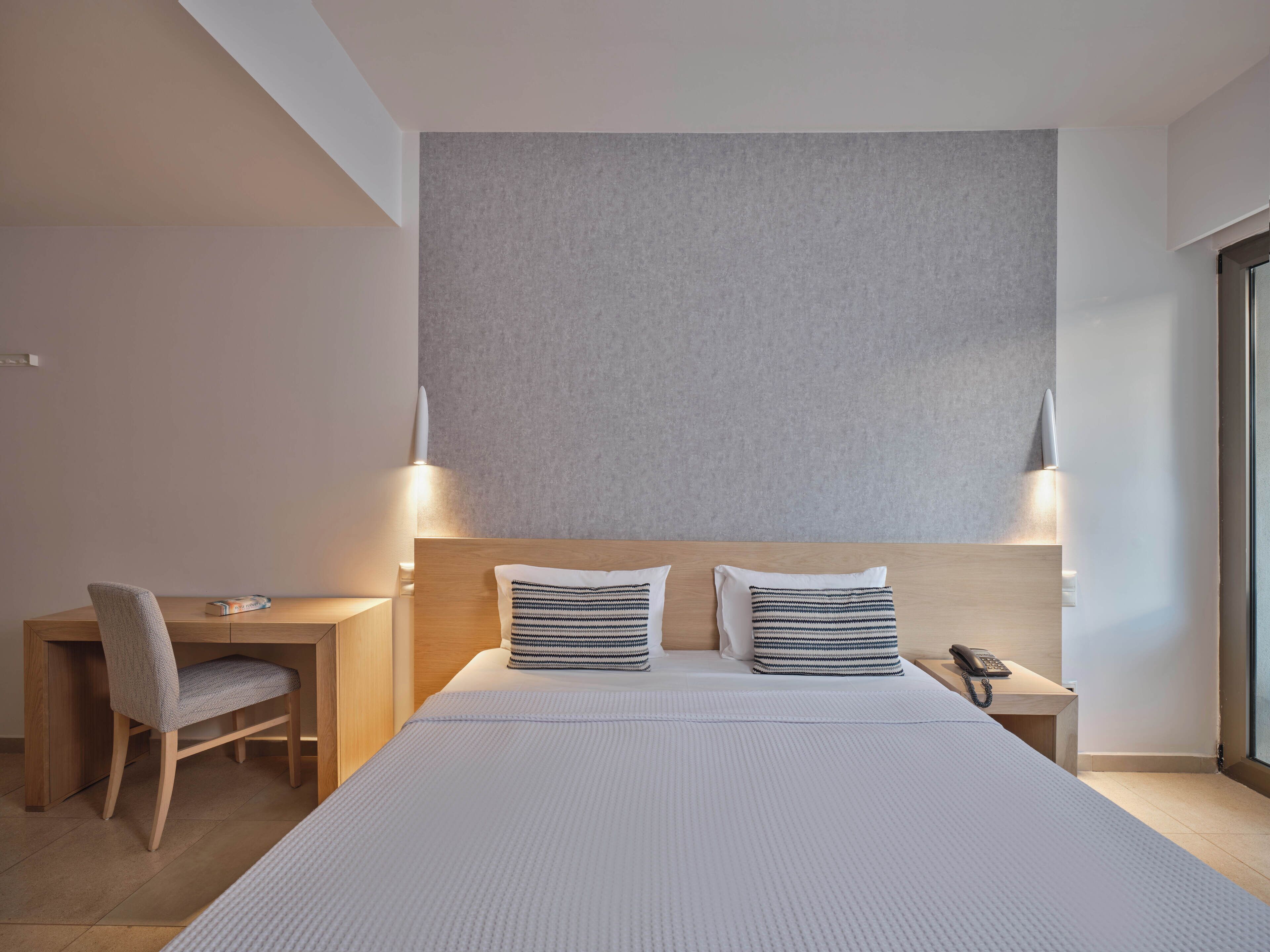 A modern hotel room with a large bed, two bedside lamps, a desk with a chair, and a telephone on the desk.