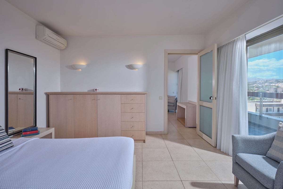 Una habitación de hotel moderna con cama, armario, escritorio y balcón con vistas.
