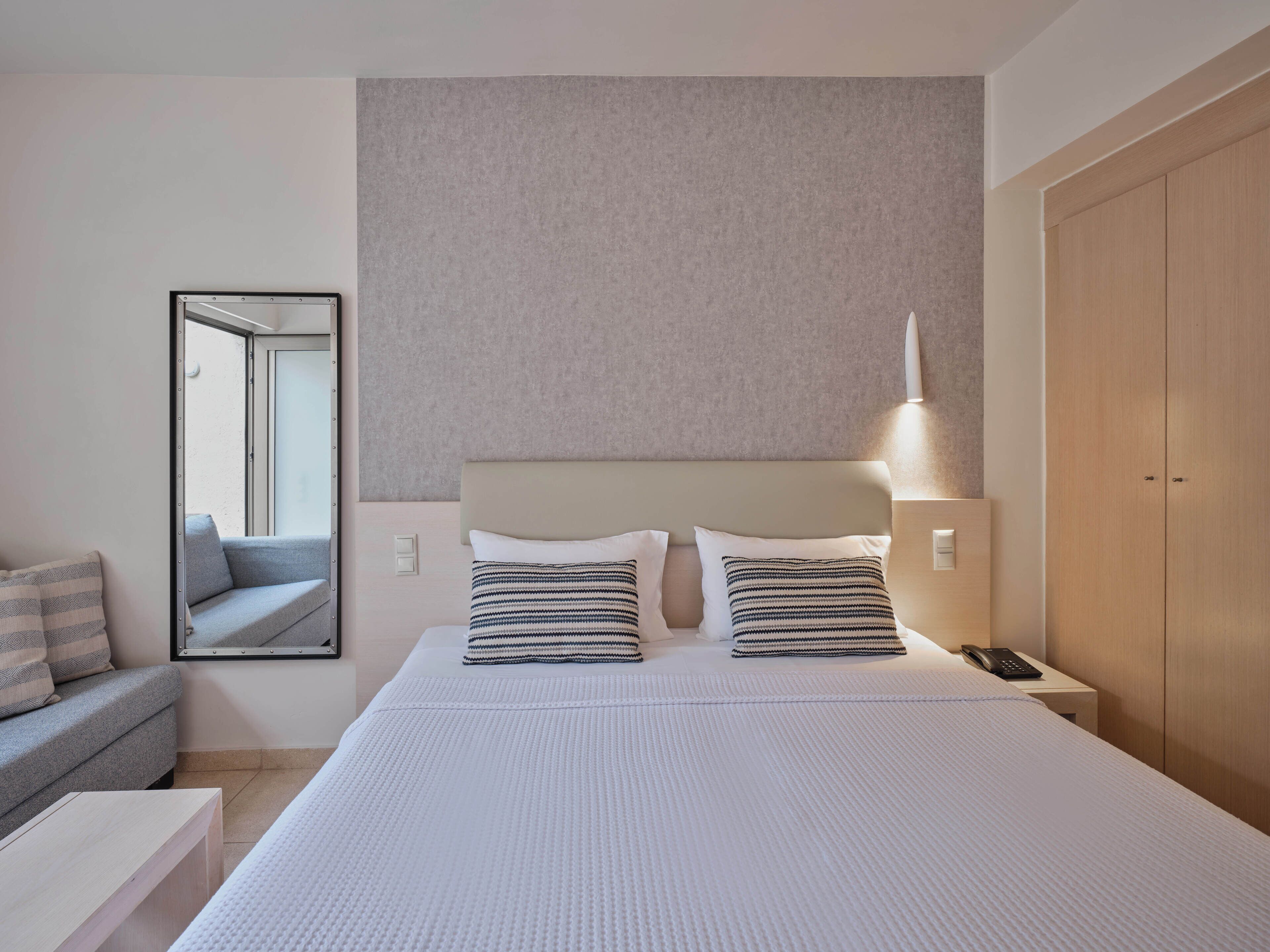 A hotel room with a large bed, two bedside lamps, a bedside phone, a sofa, and a mirror.