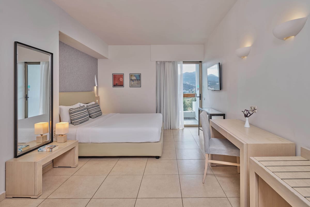 Una habitación de hotel moderna con una cama grande, un escritorio, una silla, un espejo y un televisor.