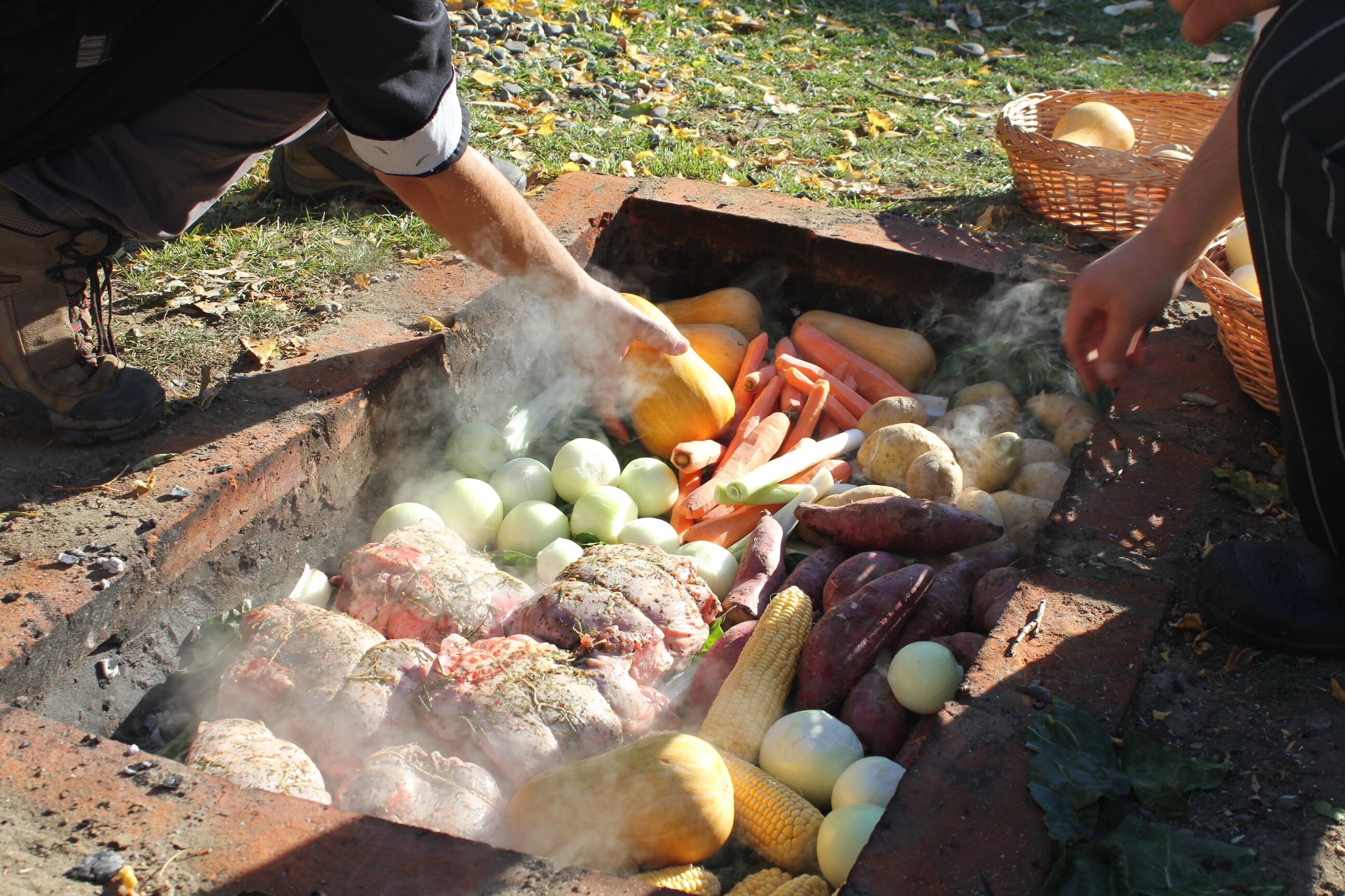 Una persona cocinando diferentes carnes y verduras a fuego abierto.