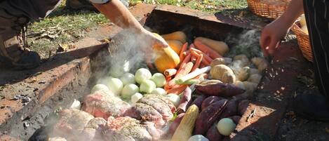 Una persona cocinando diferentes carnes y verduras a fuego abierto.
