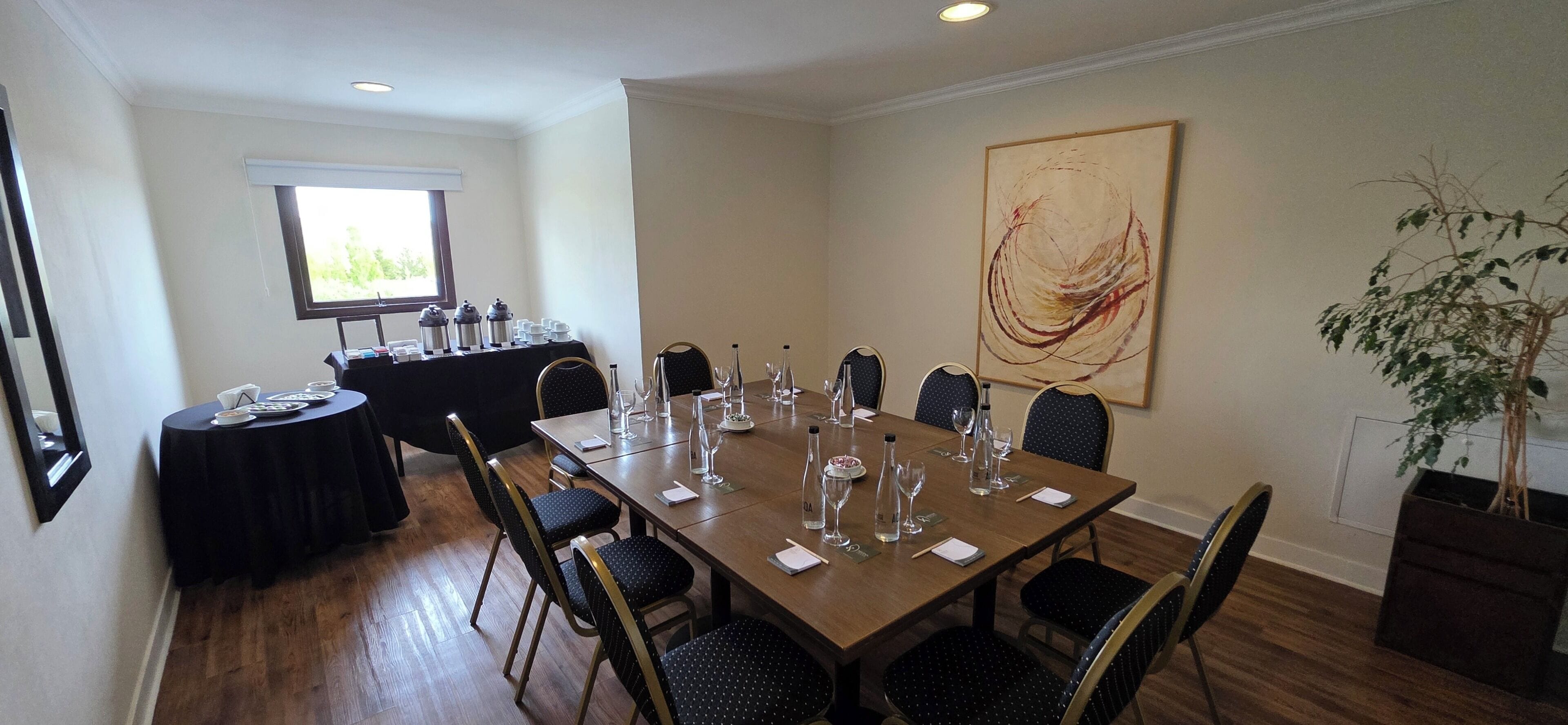 Een vergaderzaal met een lange tafel, stoelen, een koffiehoek en een groot abstract schilderij aan de muur.