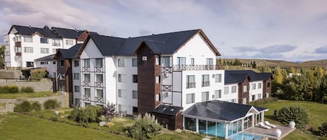 A multi-story hotel with a swimming pool, surrounded by well-maintained gardens and a hilly landscape.