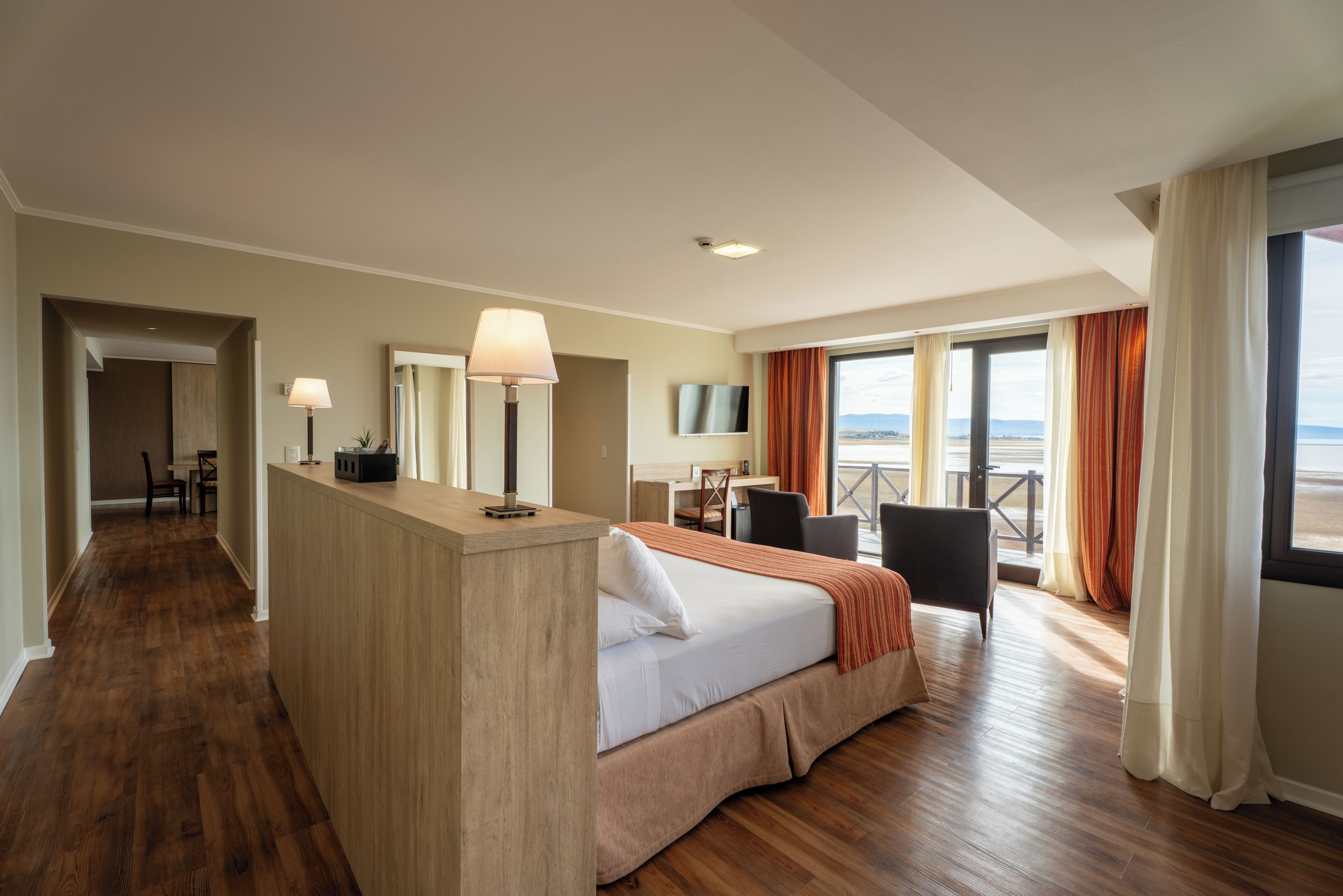 A hotel room with a bed, desk, chair, and a view of the ocean.