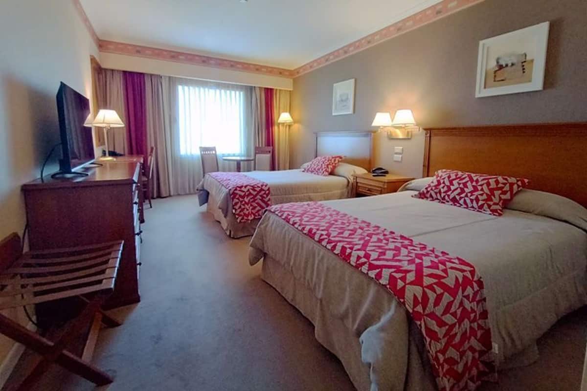 Ein Hotelzimmer mit zwei Betten, einem Schreibtisch mit Lampe, einem Sessel und einem Fernseher.