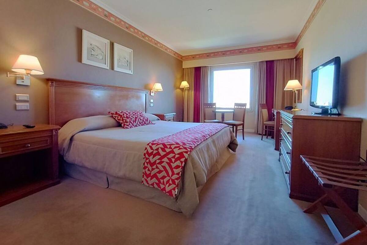 Ein Hotelzimmer mit einem großen Bett, Nachttischen, einem Schreibtisch mit Stuhl, einem Fernseher und einem Fenster mit Vorhängen.