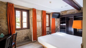 Un dormitorio con cama, escritorio de madera, cortinas naranjas, paredes de piedra y televisor.