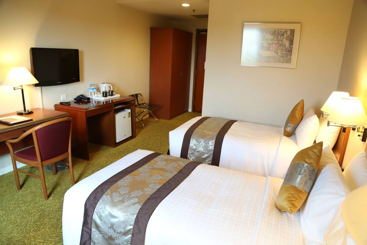 A hotel room with two beds, a desk, a chair, a television, and a coffee maker.