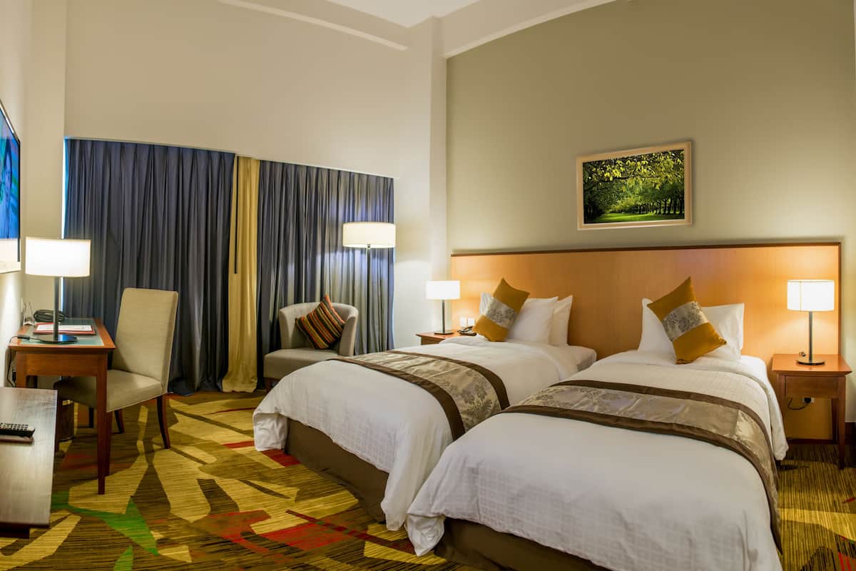 A hotel room with two beds, a desk, a chair, a TV, and a painting on the wall.
