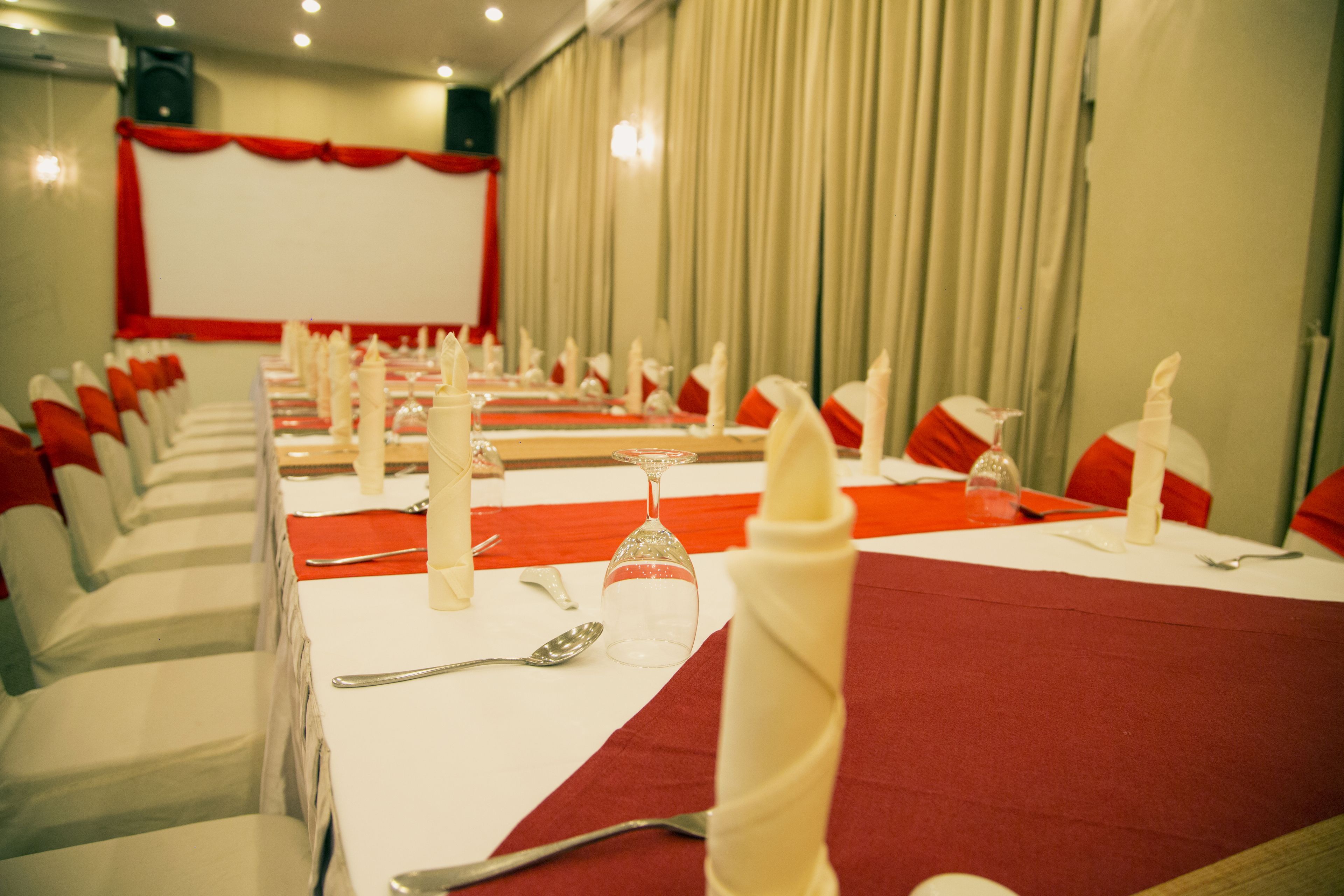 Un salón de conferencias con filas de sillas blancas, cojines rojos y un mantel rojo.