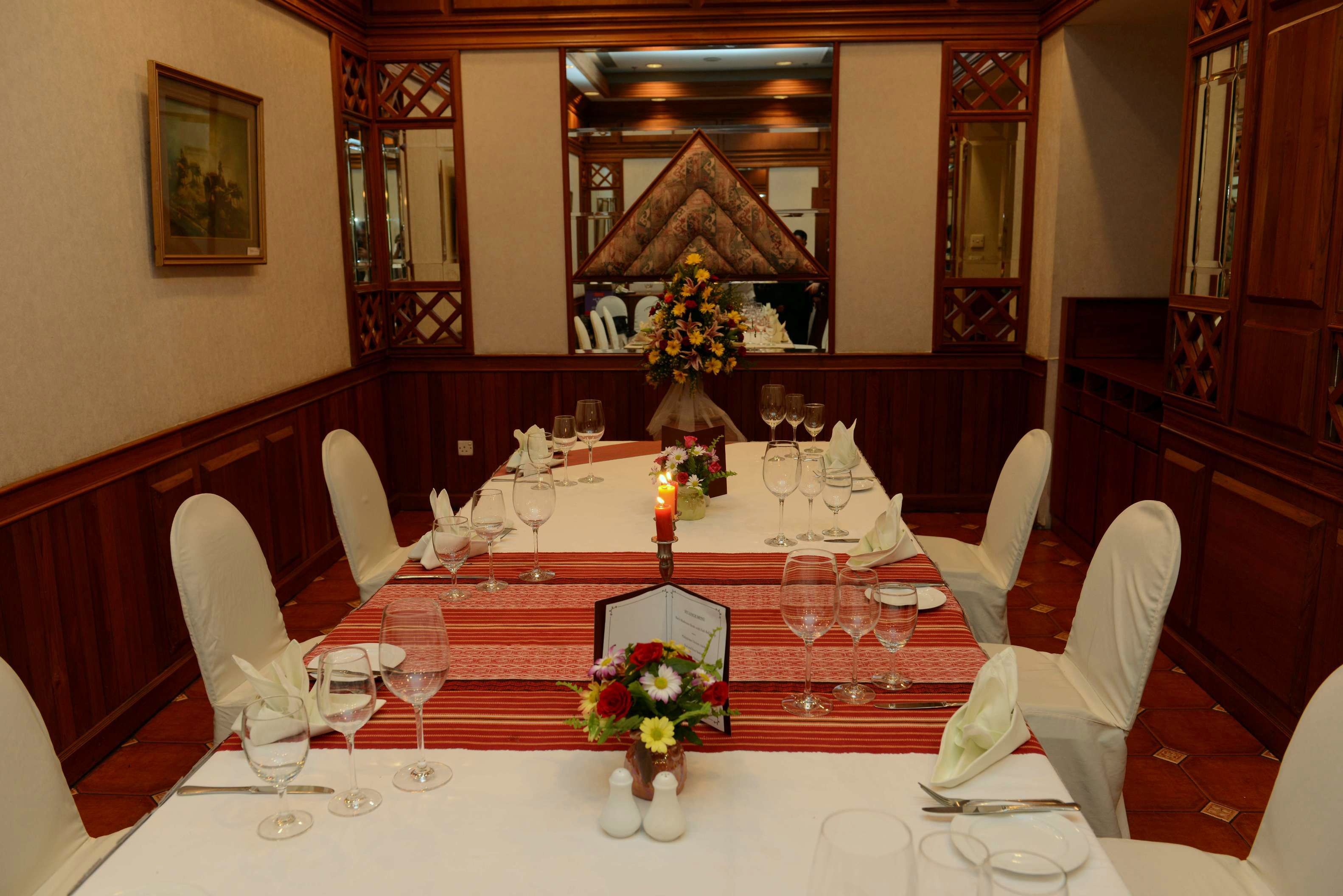 A dining room with a long table set for a meal, surrounded by chairs, with a floral centerpiece and a menu stand.