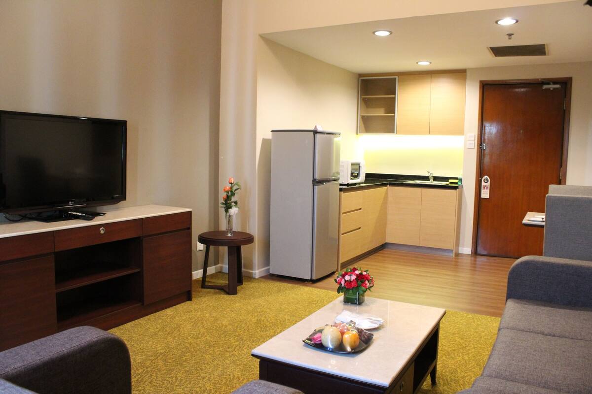 A compact living space with a flat-screen TV, a kitchenette, and a dining area with a small table and two sofas.
