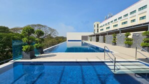 Et moderne hotel med swimmingpool, stenfacade og frodigt grønt område.