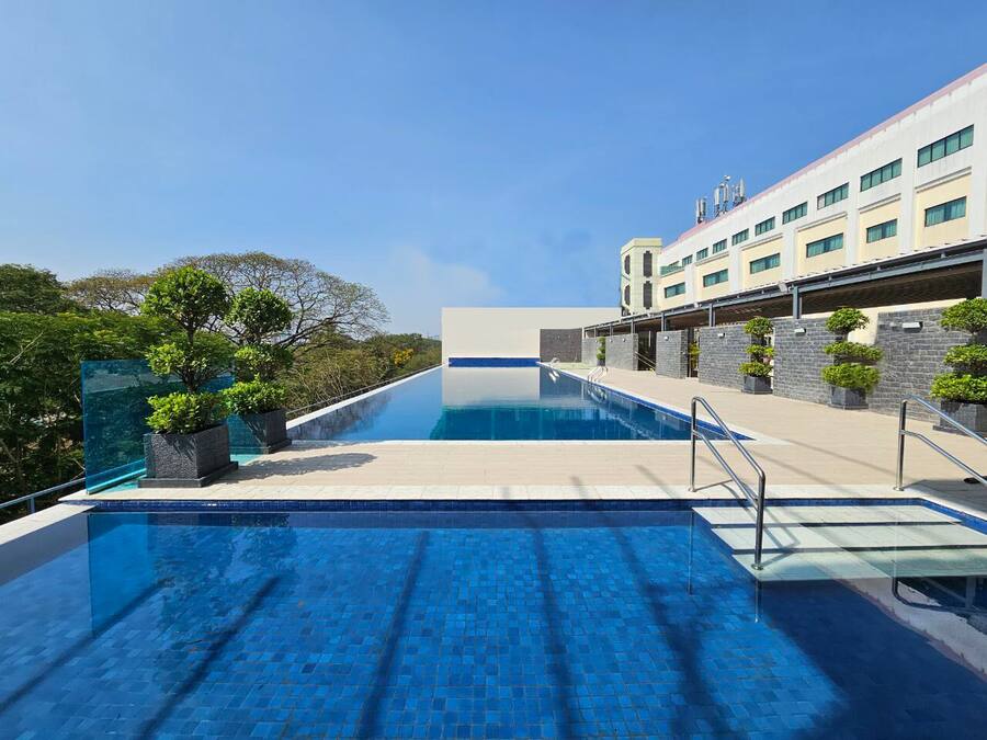 A modern hotel with a swimming pool, stone facade, and lush greenery.