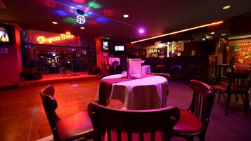A dimly lit bar area with tables and chairs, neon signage, and a stage in the background.