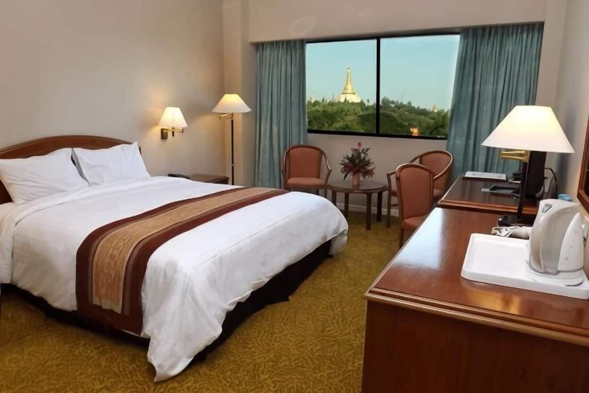 A hotel room with a bed, a desk, a chair, a lamp, and a view of a tower through the window.