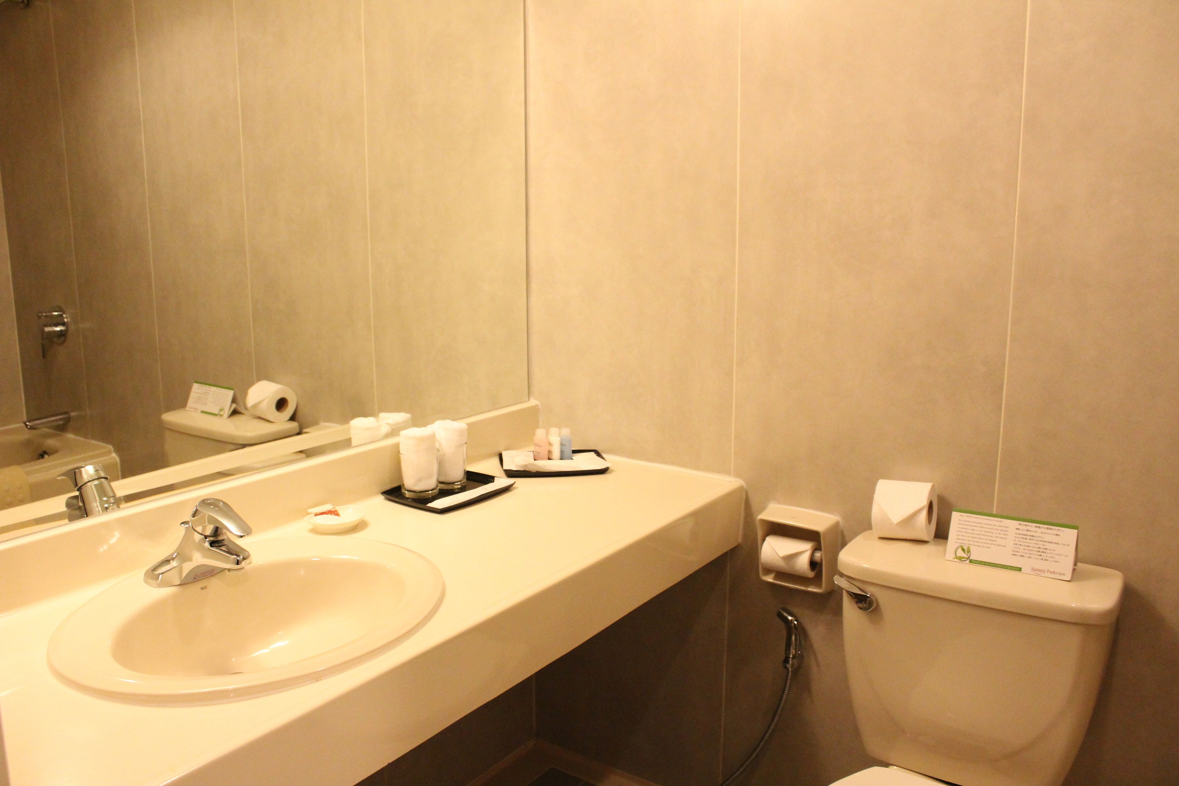 A hotel bathroom with a sink, mirror, toilet, and hand dryer.