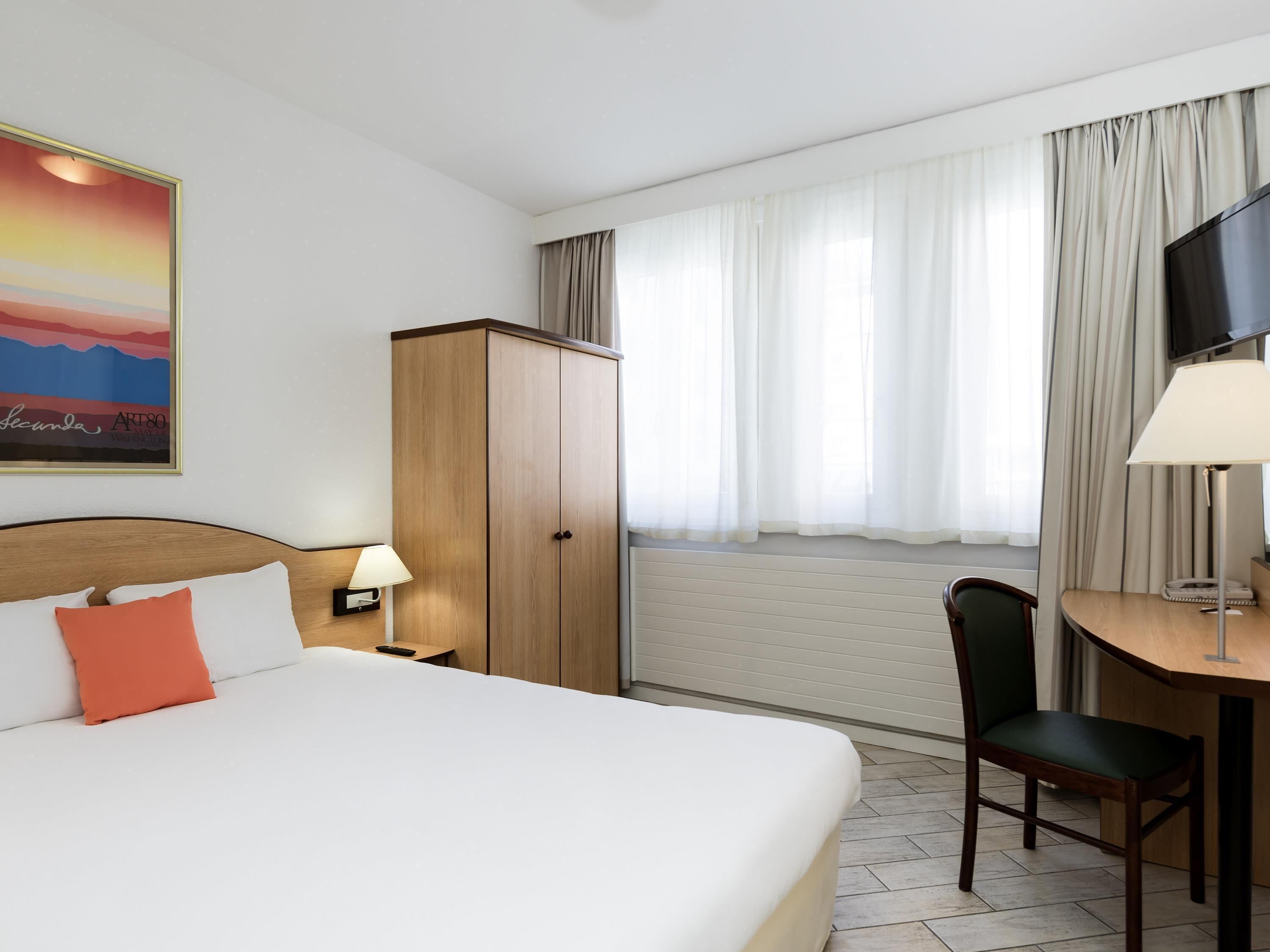 A hotel room with a bed, a desk, a chair, a TV, and a wardrobe.