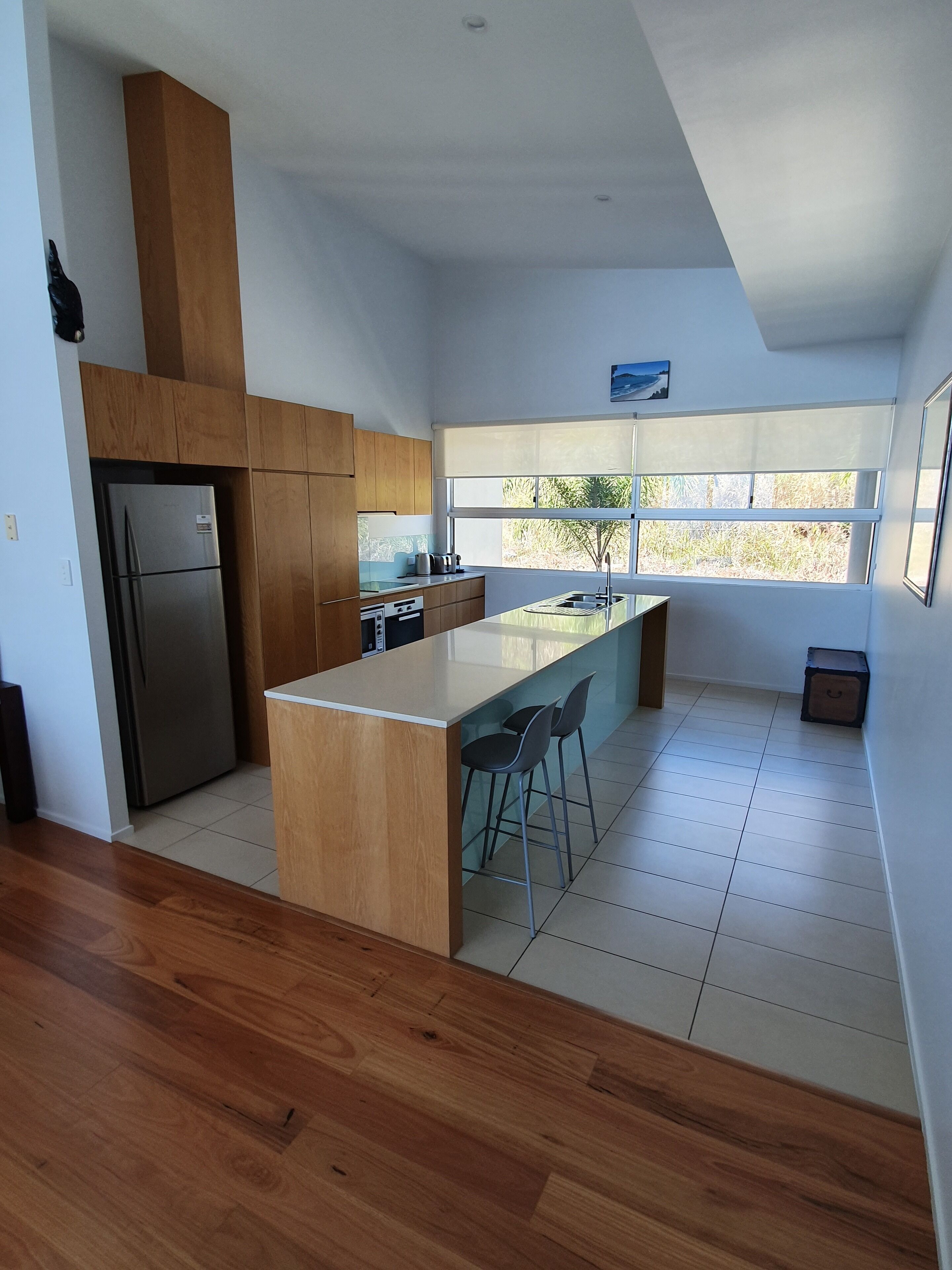A modern kitchen with a central island, wooden cabinets, and a stainless steel refrigerator.