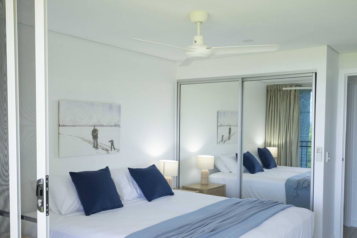 Une chambre d’hôtel avec un grand lit, un ventilateur de plafond, une table de chevet avec une lampe et un miroir.