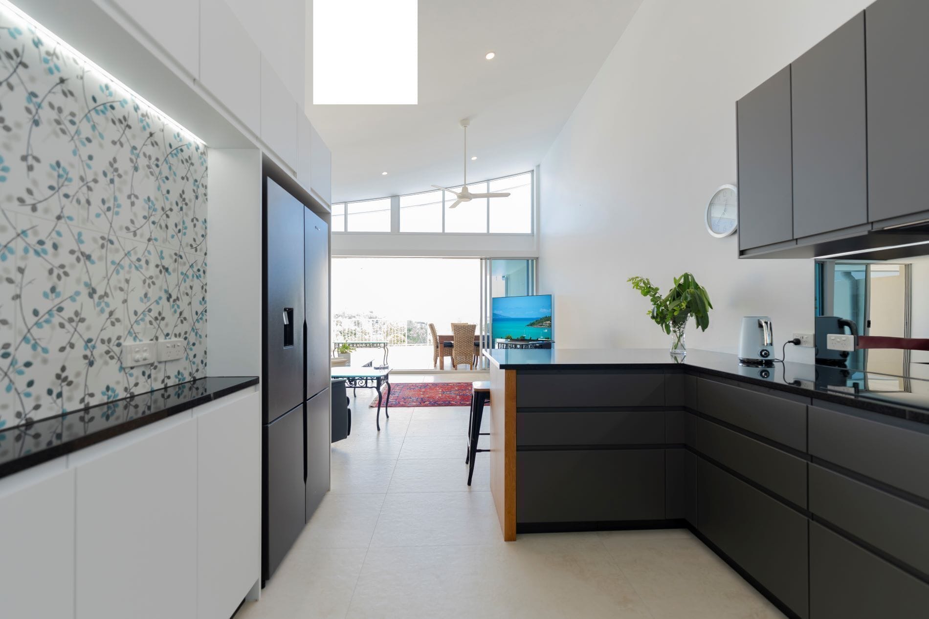 A modern kitchen with dark cabinetry, a large window, and a view of the outdoors.