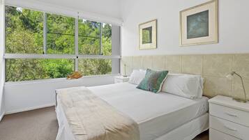 A bedroom with a large window, a bed, a nightstand, and two framed pictures on the wall.