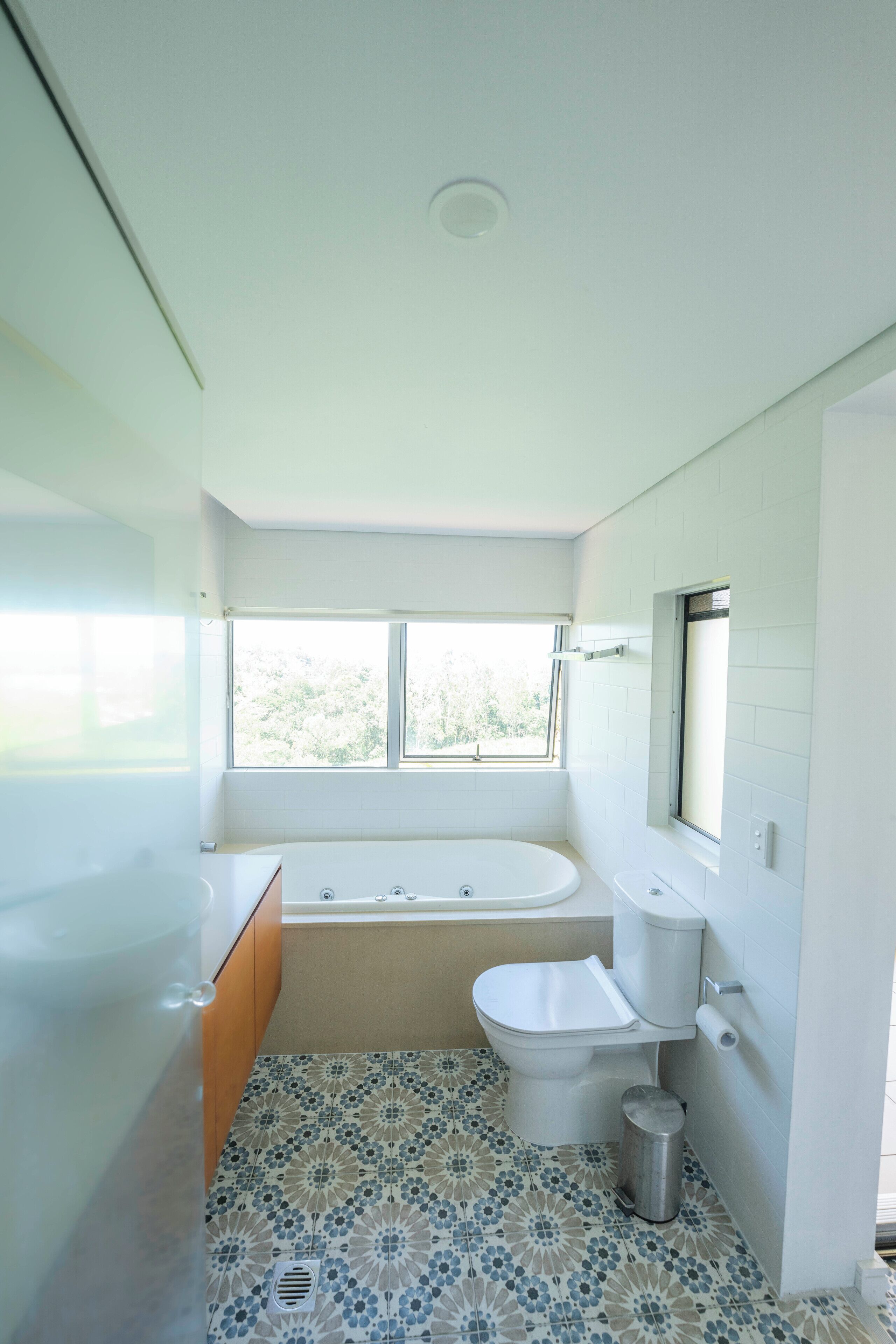 Un baño con bañera, inodoro y lavamanos. Hay una ventana sobre el inodoro y el suelo tiene azulejos estampados.
