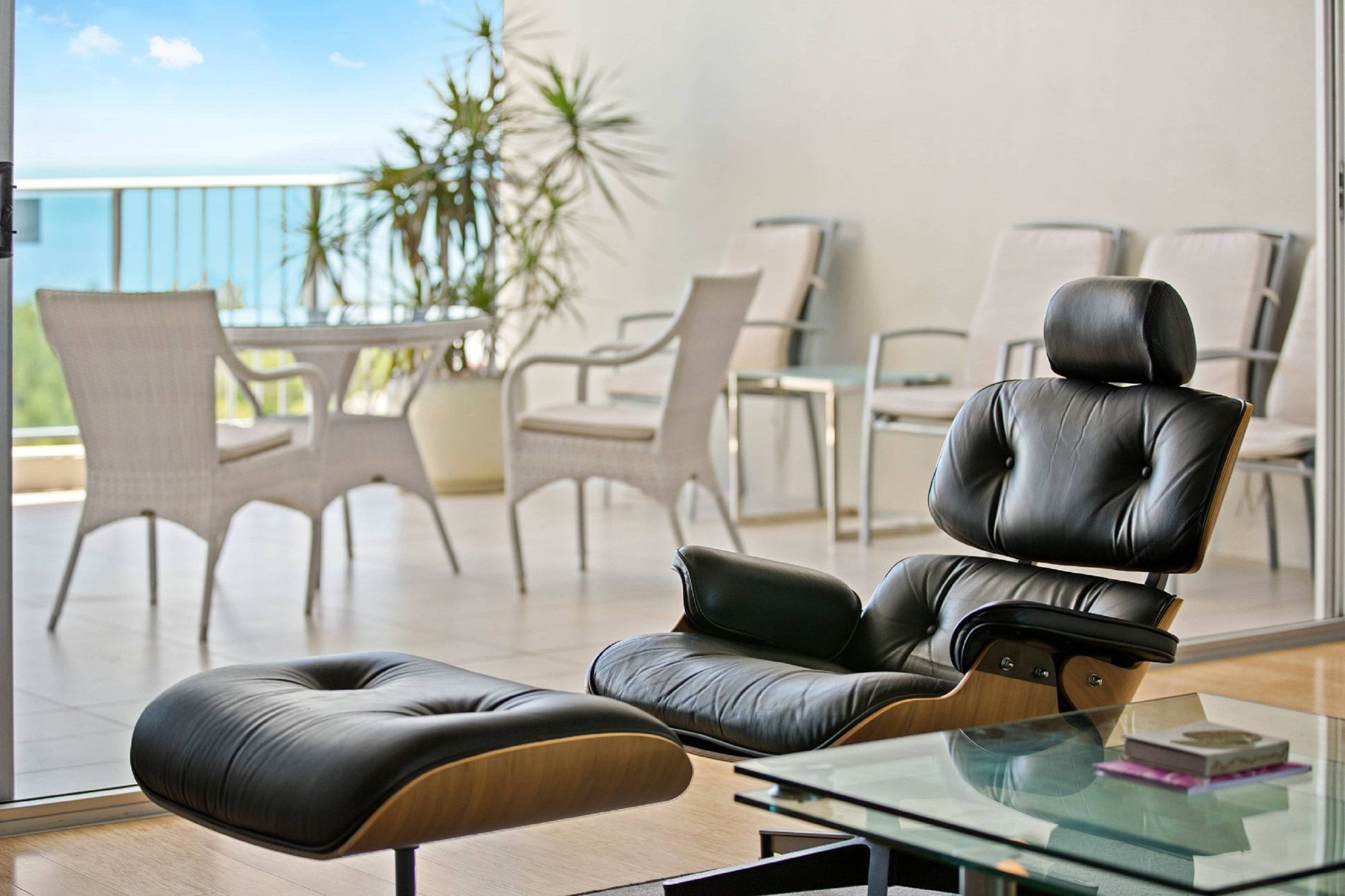 A modern living room with a glass coffee table, leather recliner, and white wicker chairs.