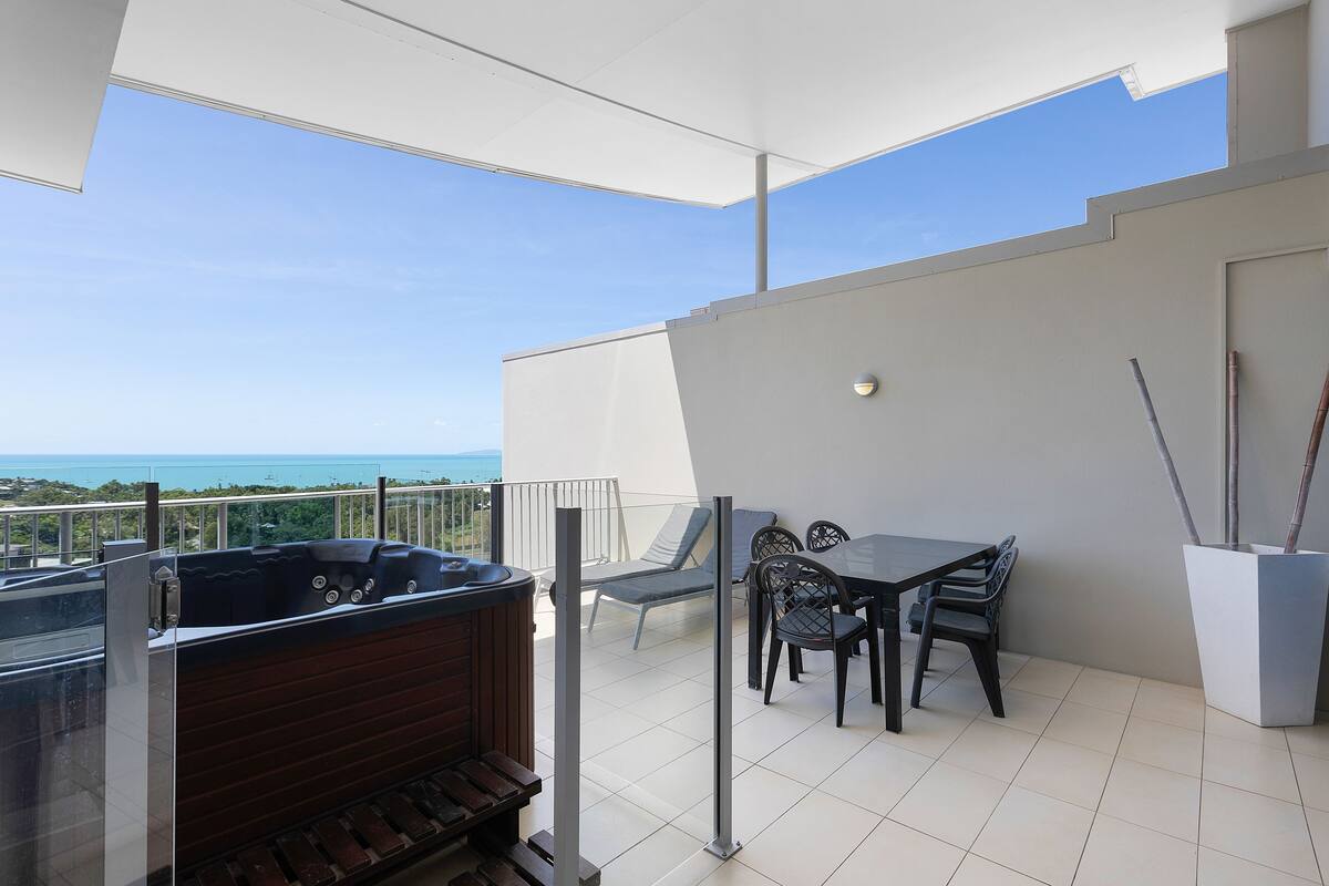 Un balcon avec un jacuzzi, une table et des chaises, et une vue sur l’océan.