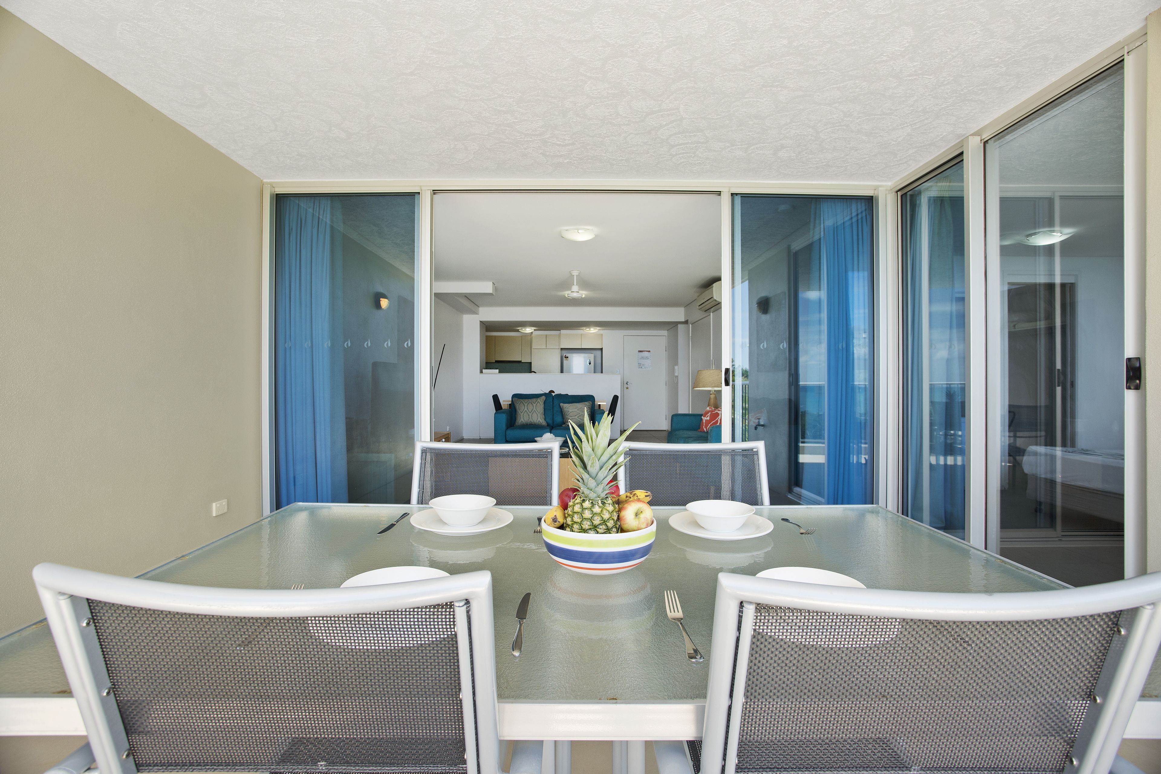 A dining area with a glass table, white chairs, and a fruit bowl.