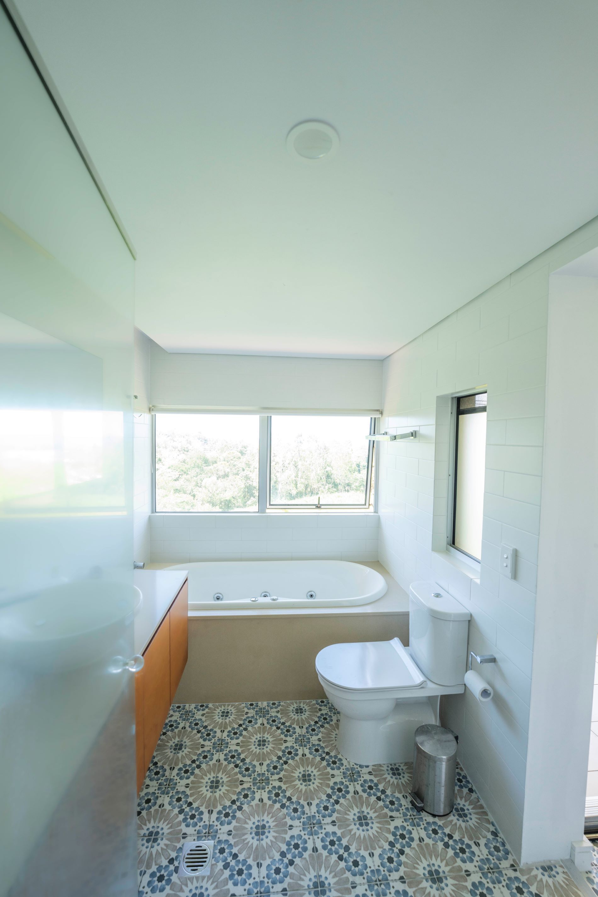 Ein Badezimmer mit Badewanne, Toilette und Waschbecken, mit Fenster und Fliesenboden mit Muster.