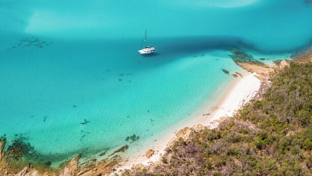 Een kustlandschap met een heldere turquoise zee, een zandstrand en een zeilboot.