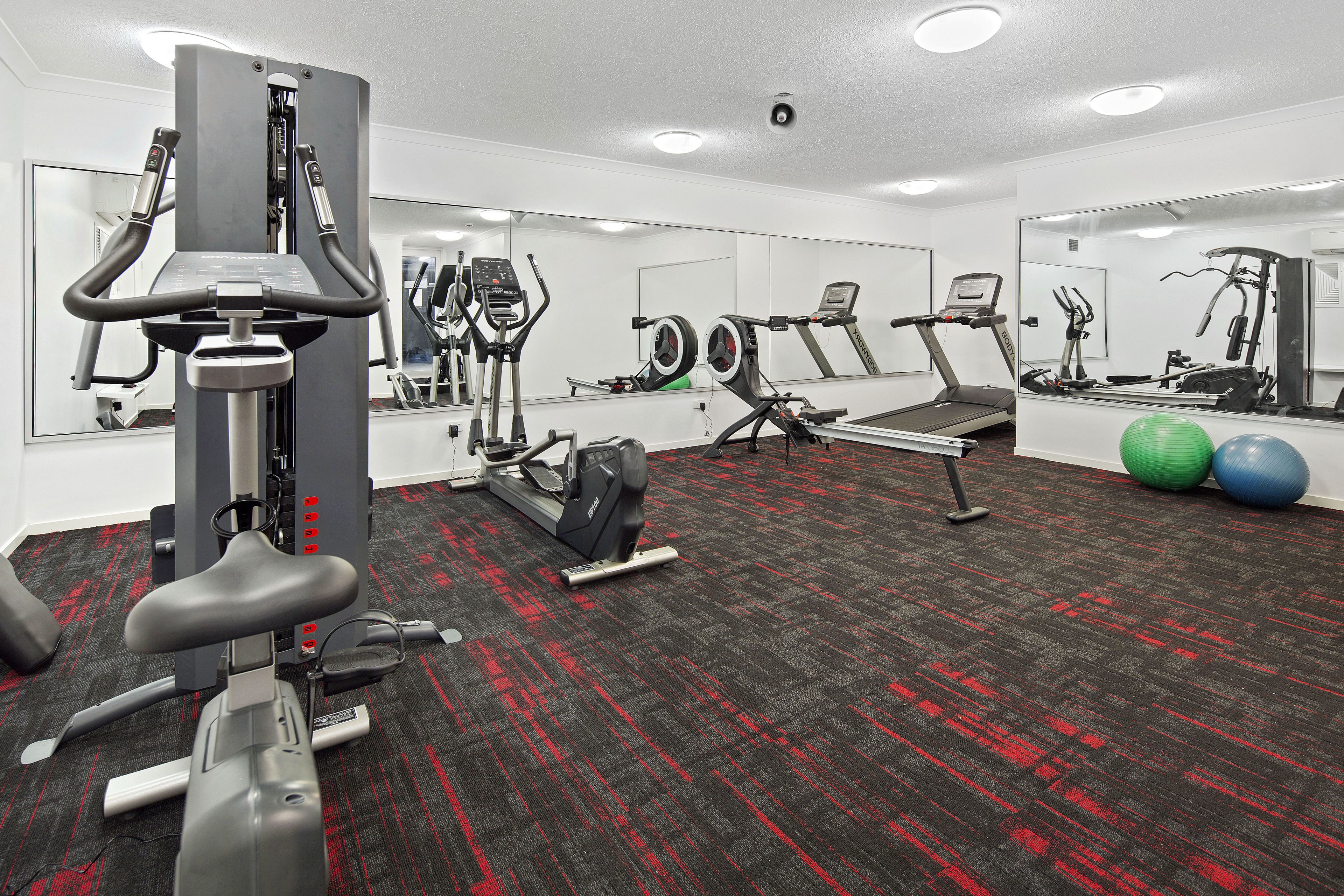 Een sportschool met trainingsapparatuur, een spiegelwand en een vloerbedekking.