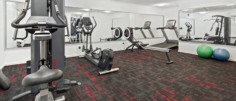 Een sportschool met trainingsapparatuur, een spiegelwand en een vloerbedekking.