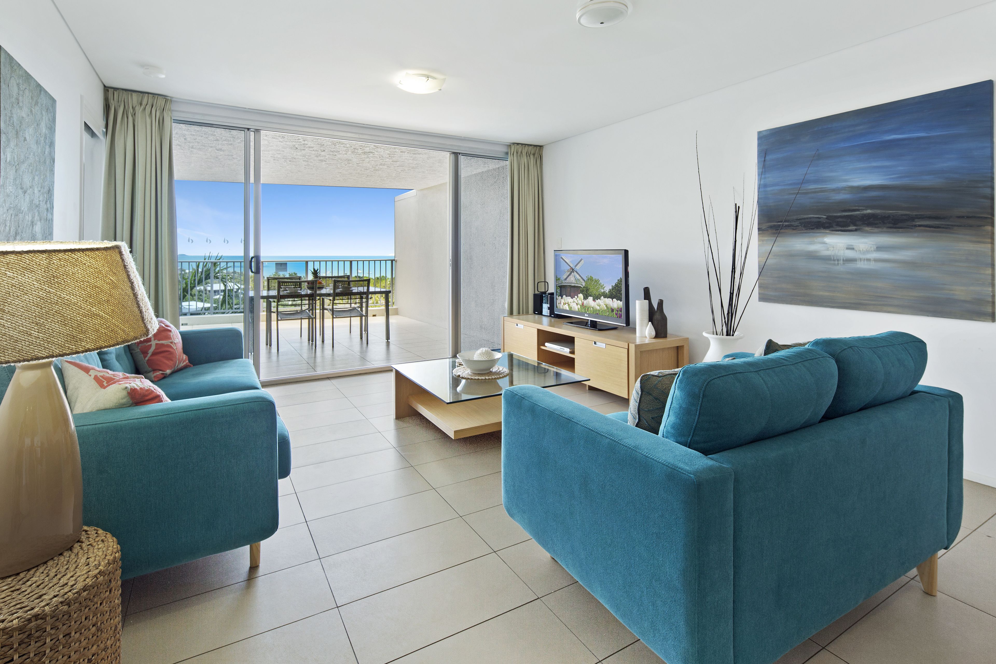 Ein modernes Wohnzimmer mit einer Couch, einem Couchtisch und einem Fernseher. Es gibt einen Balkon mit Blick auf das Meer.
