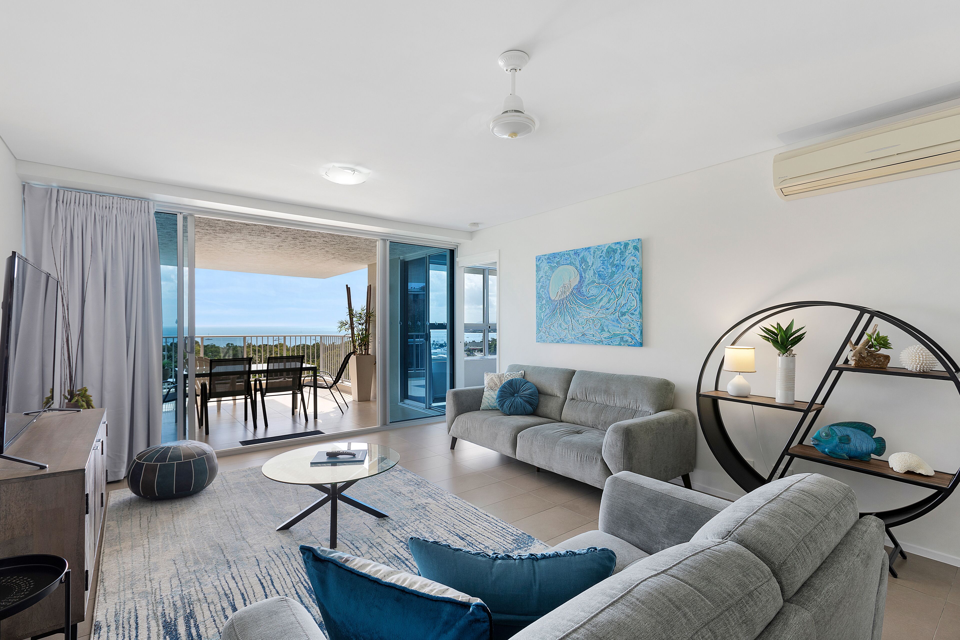 A modern living room with a grey sofa, a round coffee table, and a view of the ocean through large sliding doors.