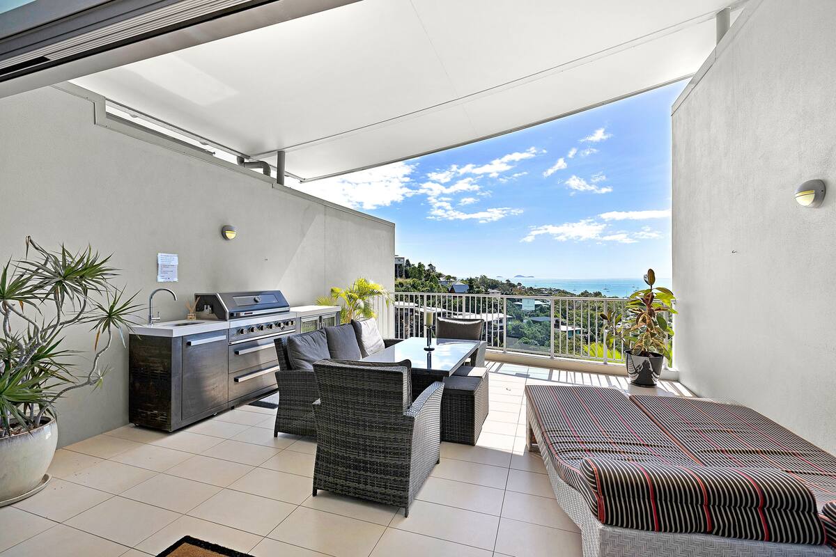 Un balcon avec un barbecue, des sièges et des plantes en pot.