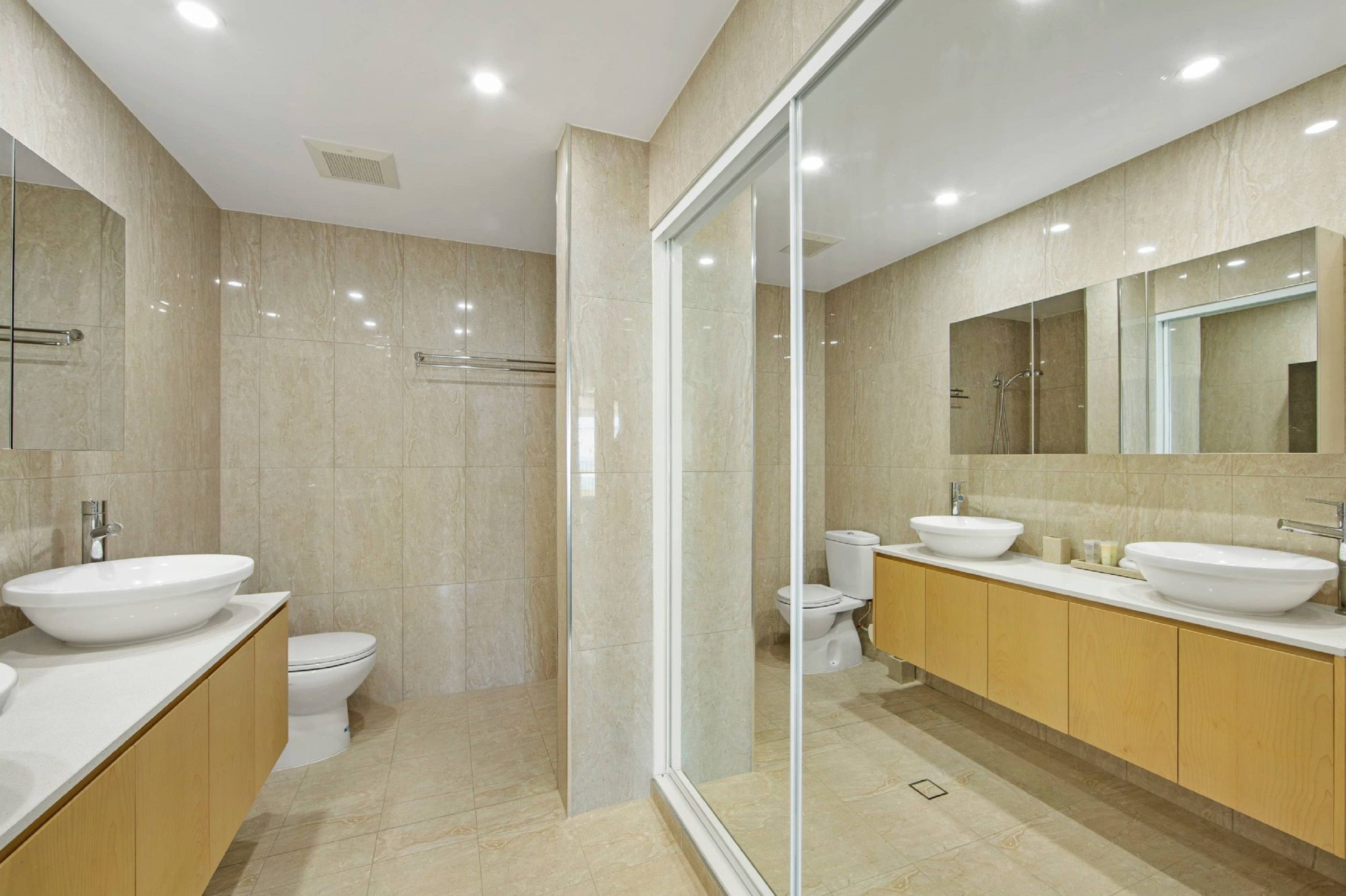 A modern bathroom with a large mirror, two sinks, and a shower area.