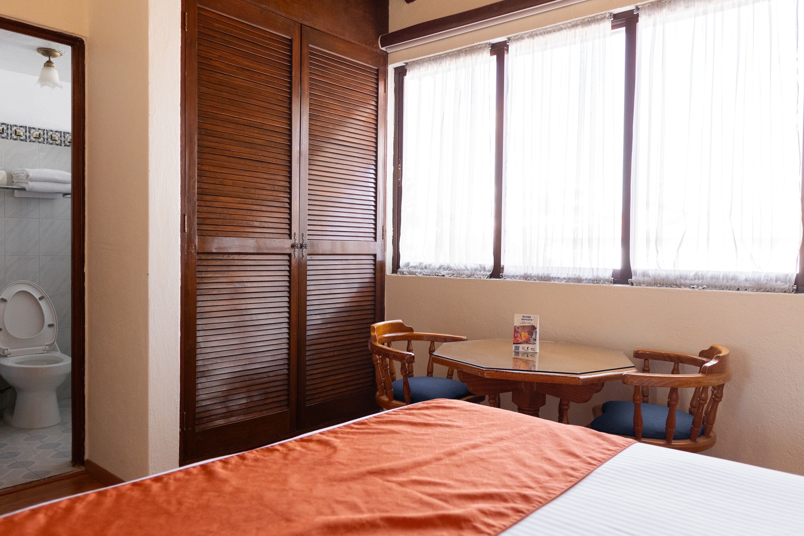 Habitación de hotel con cama, armario de madera, inodoro y ventana con cortinas.