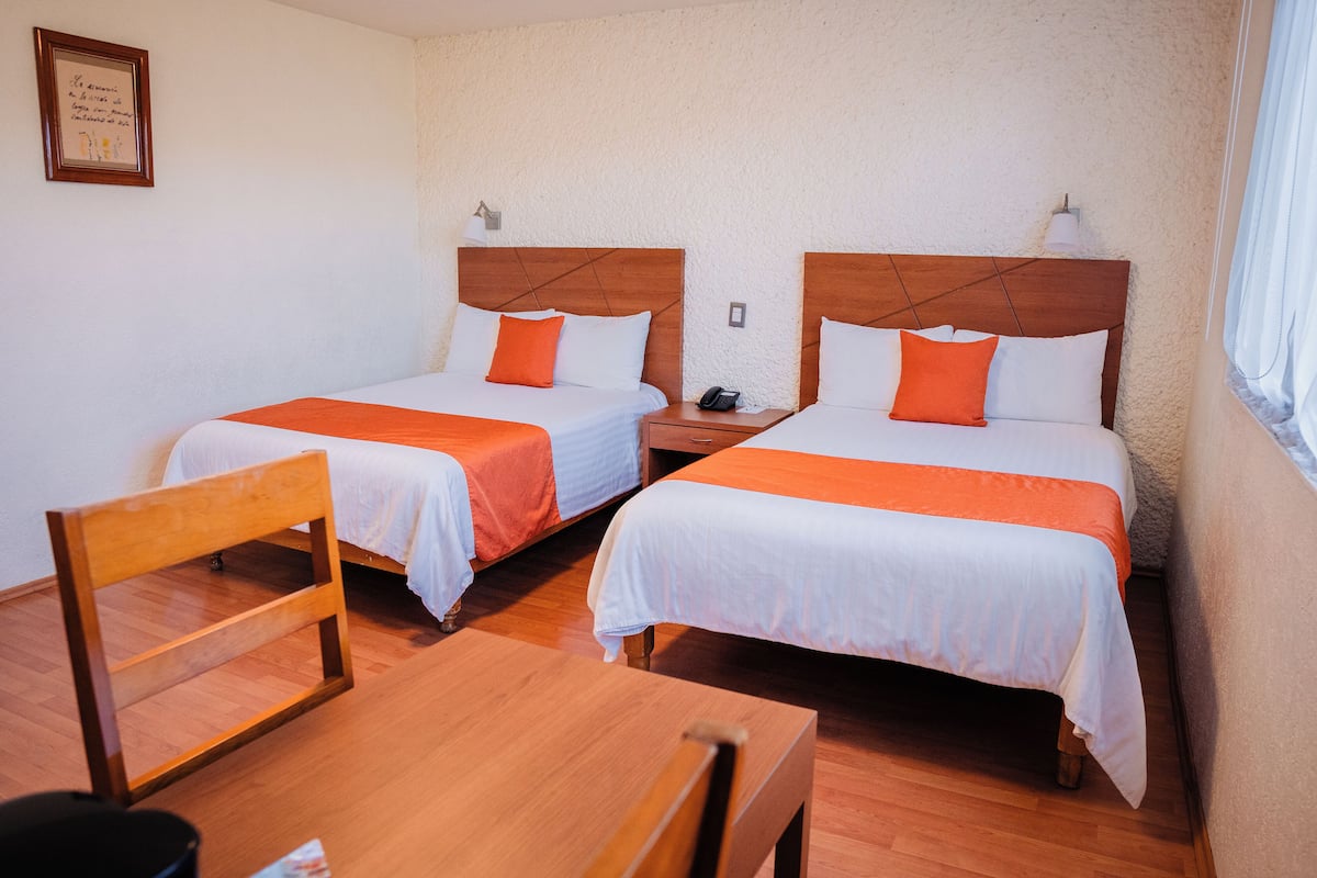 A hotel room with two single beds, wooden headboards, white bedding, and orange accents.