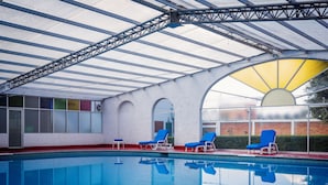 Ein Schwimmbecken mit blauen Liegestühlen und einem überdachten Bereich mit Glasdach.