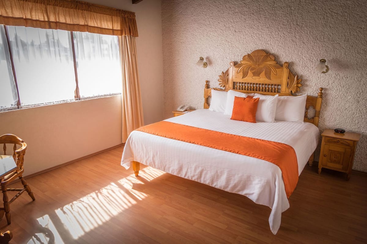 A bedroom with a large bed, wooden headboard, a nightstand, a chair, and a window with curtains.