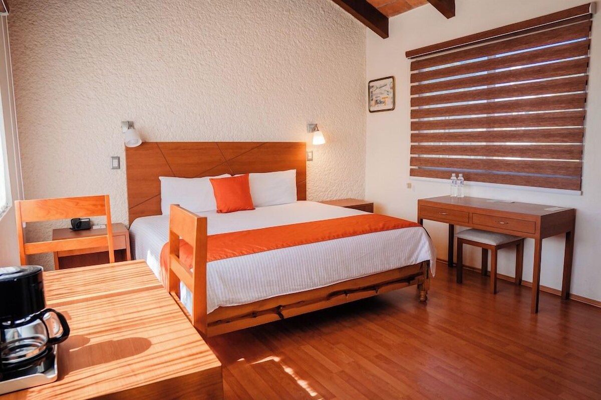 Quarto com cama de madeira, escrivaninha, cadeira, mesa de cabeceira e cafeteira.