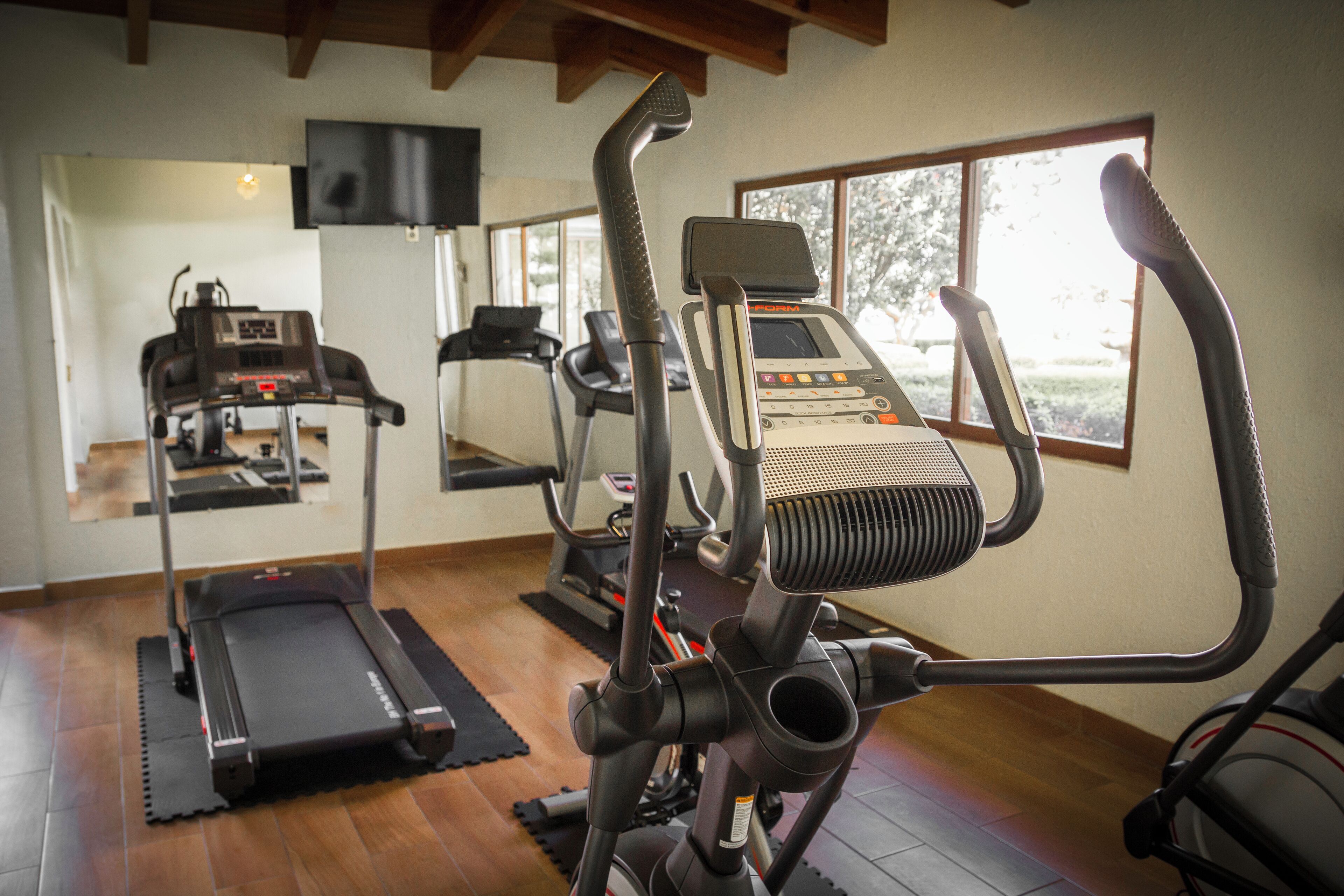 Un gimnasio en casa con cinta de correr, elíptica y bicicleta estática.